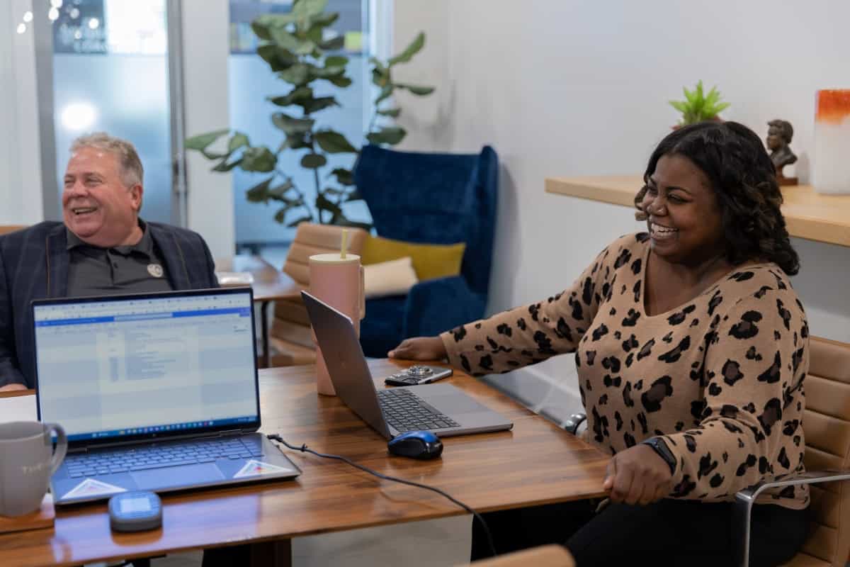 Two people sitting at a home table with laptops in front of them.